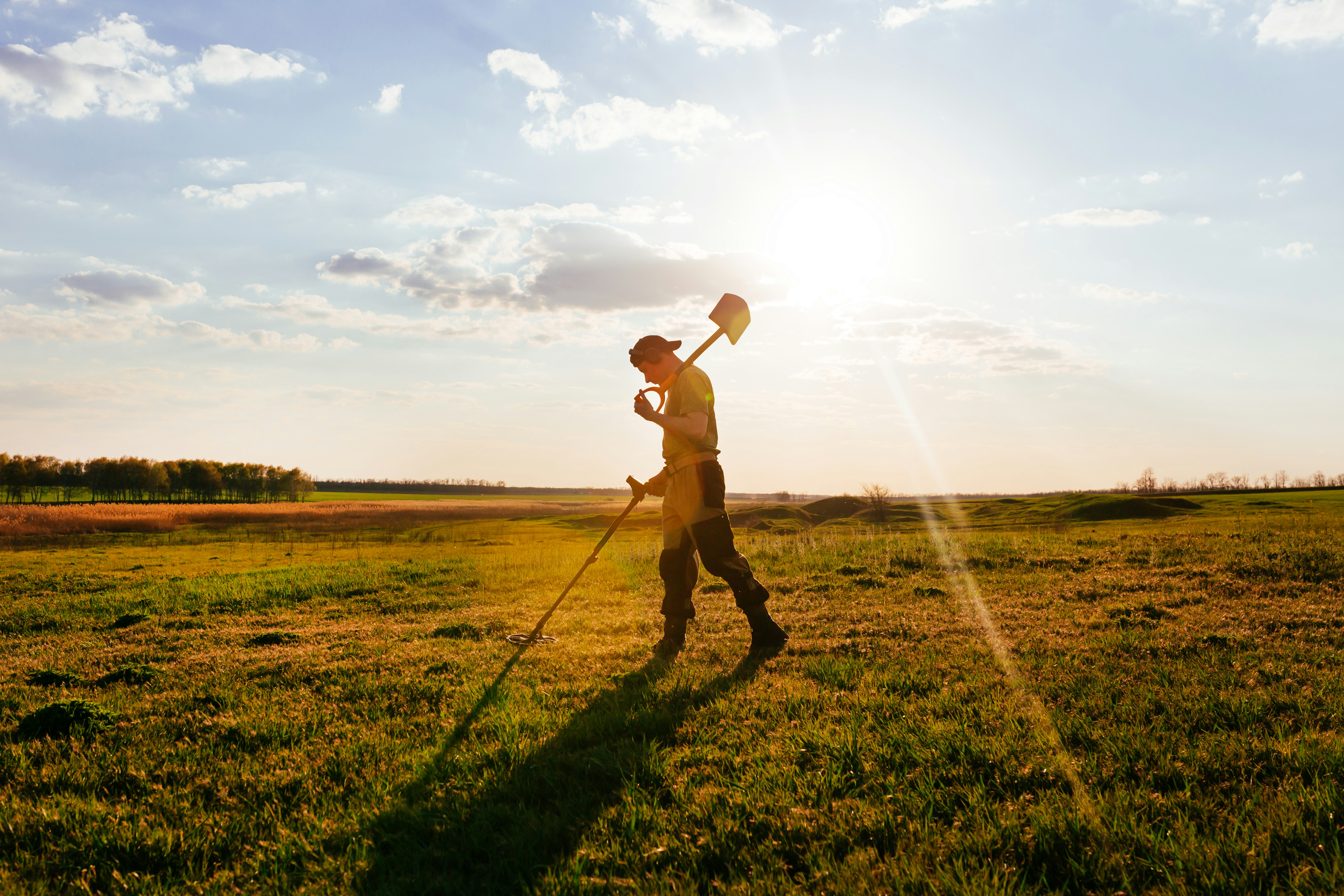 Prospector scanning open grassland with a metal detector at sunset